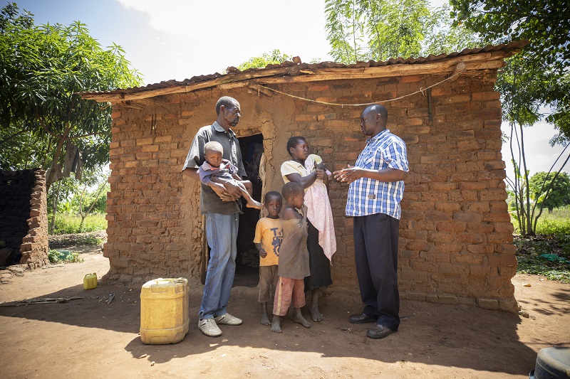 A middle aged man speaks with a family in need in front of their hut in Uganda.