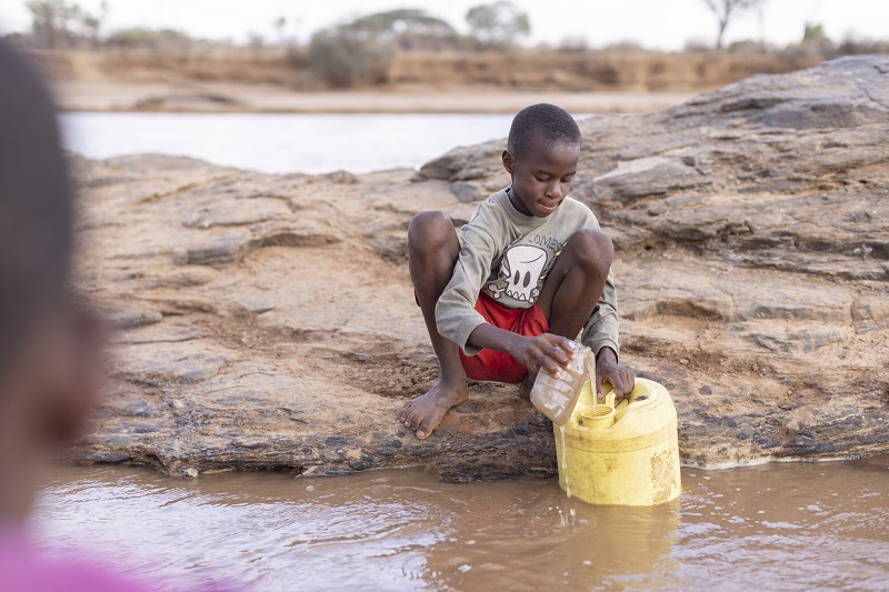 Boy draws water from a dirty river in Kenya.