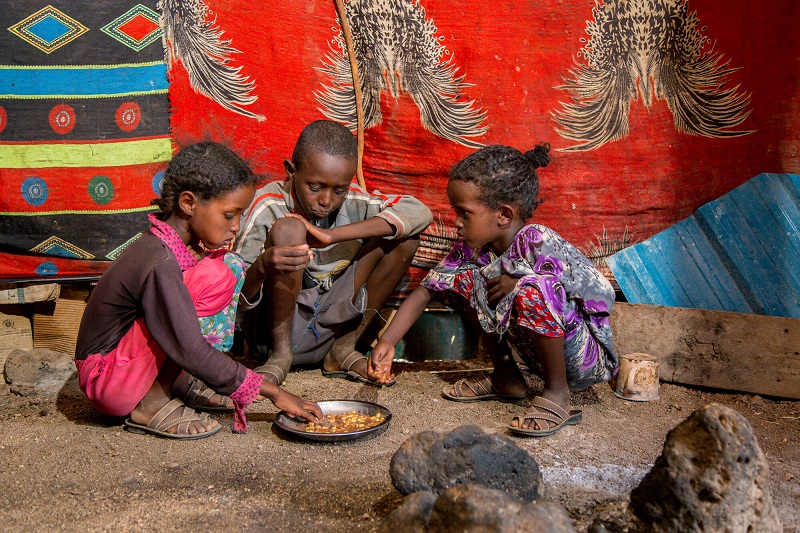 Children eat together from a small bowl of maize in Kenya.