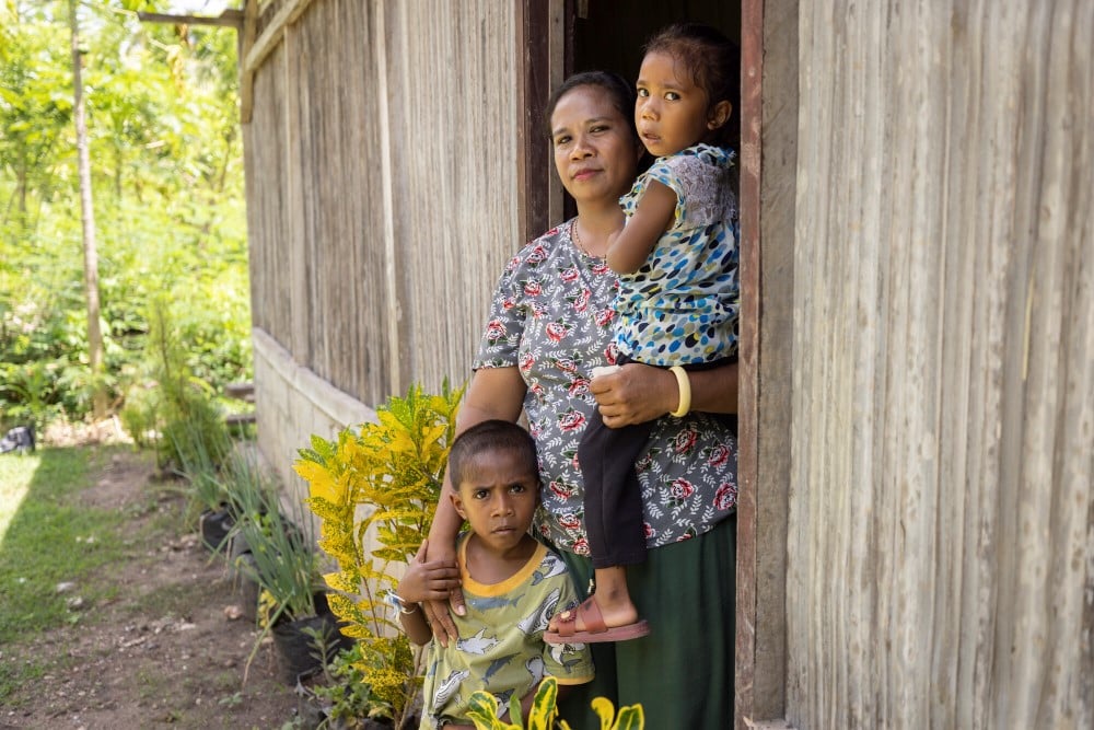 Mother in Indonesia stands in a doorway with her two children.