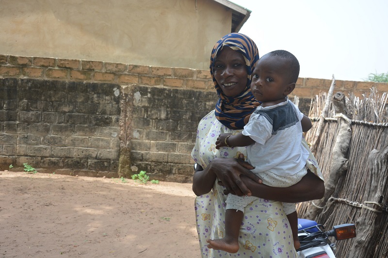 A mom in The Gambia smiles at the camera while holding a baby.