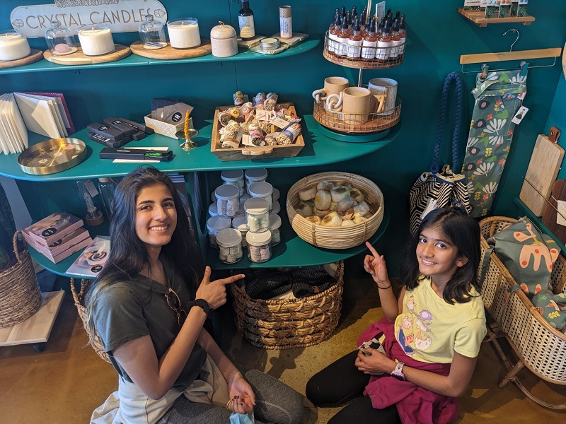 Two young girls smile in front of a shelf of handmade goods