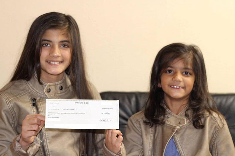 Two young girls hold up a cashier's check, smiling