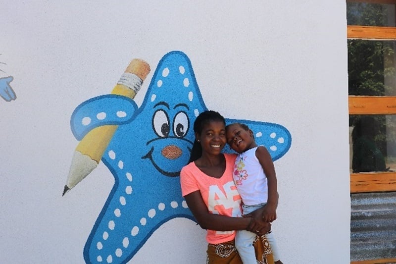 A mom and child smile in front of an ECD center.