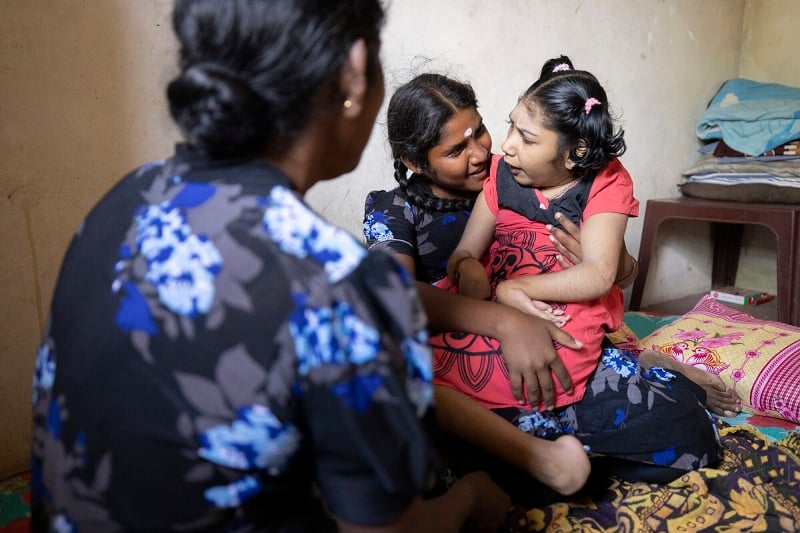 A mom holds her disabled daughter on a mattress in Sri Lanka as they chat with a ChildFund representative.