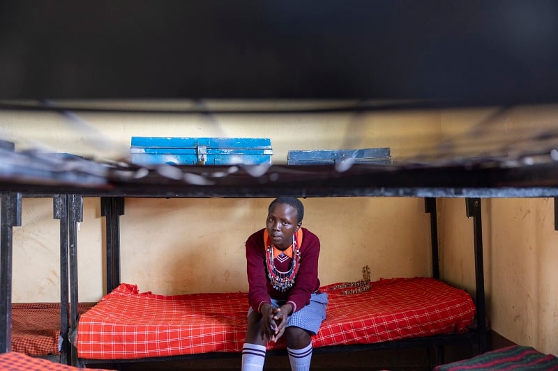 A teenage girl in Kenya sits on a dormitory bed.