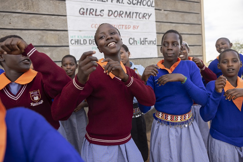 A teenage girl in Kenya dances with a group of other girls.