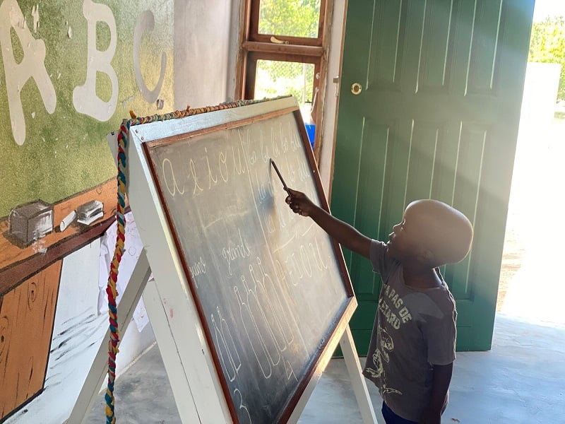 A young boy in Mozambique points to a blackboard with letters on it.