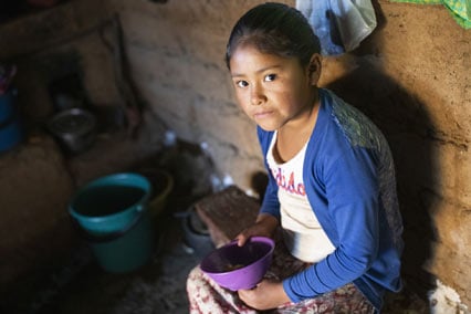 Girl in Bolivia sits inside holding empty bowl.