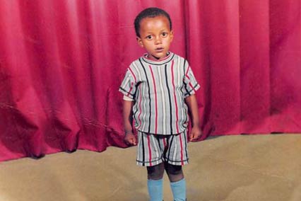 Boy child standing in front of red curtain in Ethiopia