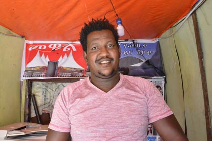 Man standing outside of shop in Ethiopia smiling in front of a sign in Amharic.