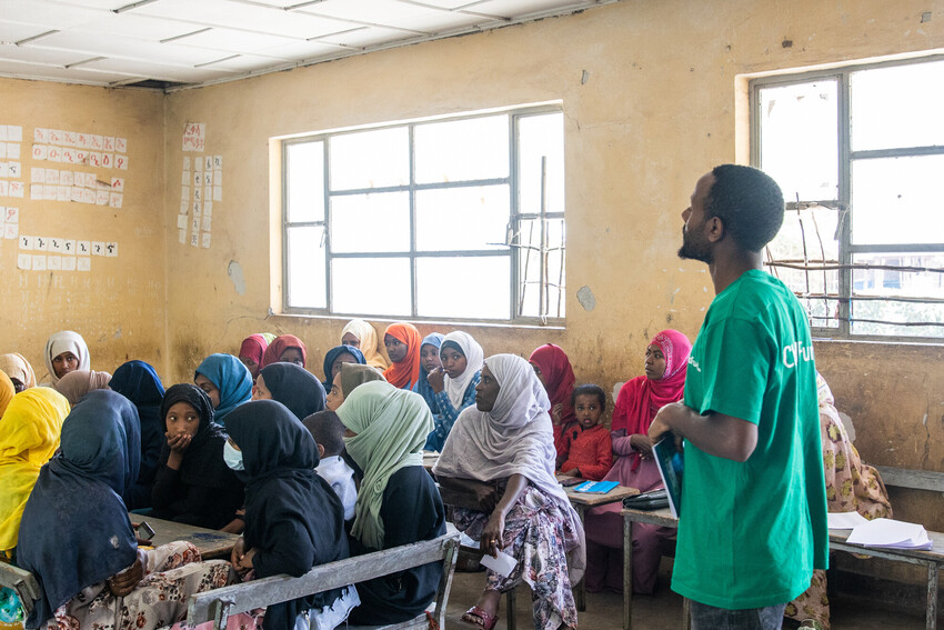 A ChildFund staffer stands in a classroom in front of a room full of youth.