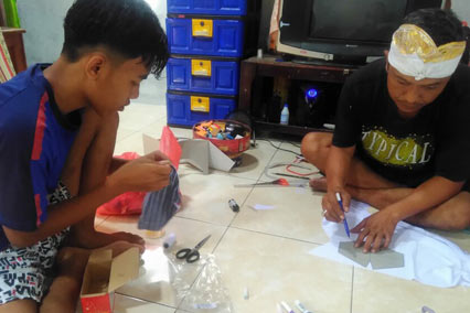 Boy and father sit inside making facemasks in Indonesia.