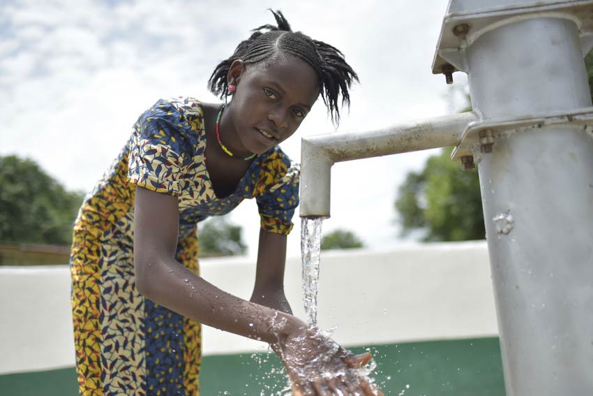 Girl washes hands at water well outside smiling in Sierra Leone.
