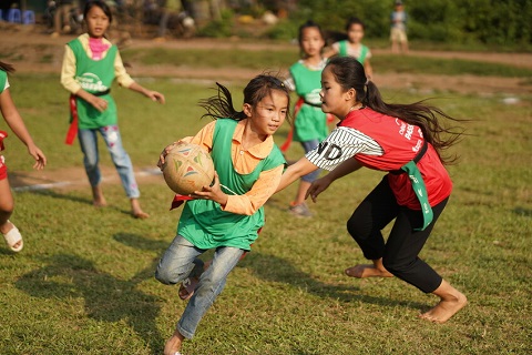 A girl in a green jersey plays rugby in Vietnam.