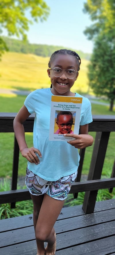 Young girl in Virginia smiles in front of the camera, holding a photo of her sponsored child in Zambia.