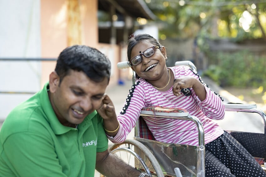 Girl in wheelchair in Sri Lanka laughs with a ChildFund staff member.