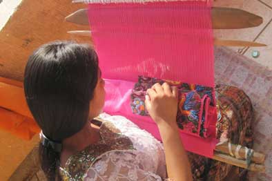 girl sitting on ground holding thread, pink fabric, weaving