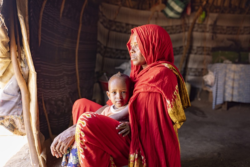 A woman in Kenya sits on the floor of her home with her daughter, looking into the distance.